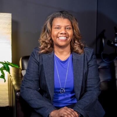 Cristi Ford, a Black woman wearing a blue shirt under a darker blue blazer and a long necklace.