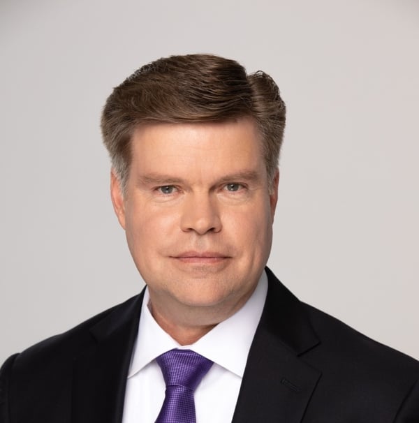 Jason Palmer, a light-skinned man with brown hair, with a touch of gray at the temples, wearing a black suit with a white shirt and purple necktie