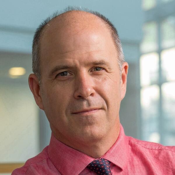 Jim Lang, a light-skinned man wearing a pink collared shirt and tie.