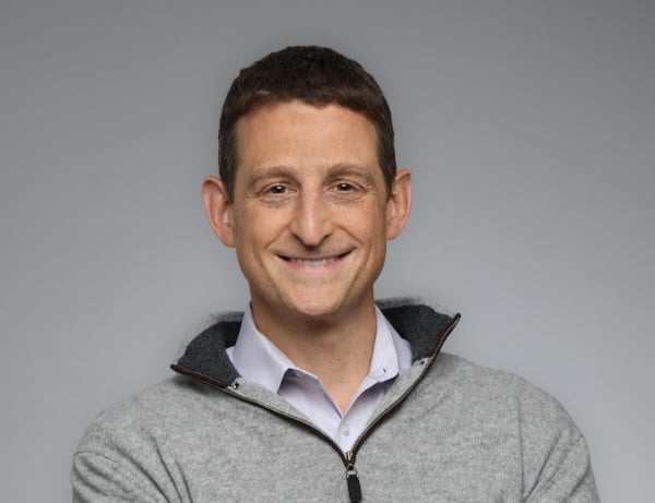 A light-skinned man with short dark hair wearing a half-zip fleece over a collared shirt.