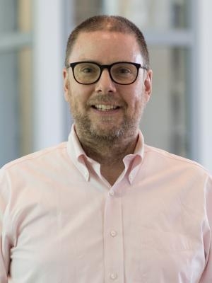 Wendel Cox, a light-skinned man with short hair, a beard, and mustache, wearing glasses and a peach button-down shirt.