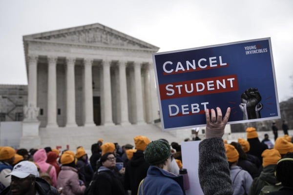 A demonstrator holding up a sign that says "Cancel Student Debt" in a crowd of people in front of the Supreme Court building