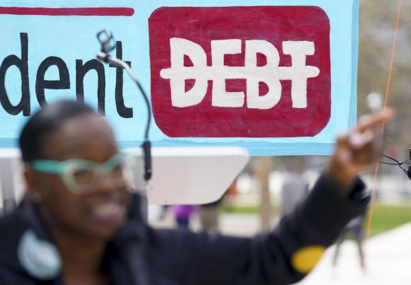 A demonstrator in front of a sign with the word "debt" crossed out.