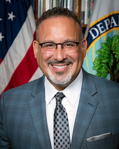 Secretary of Education Miguel Cardona, a middle-aged Hispanic man with glasses and a salt-and-pepper goatee.