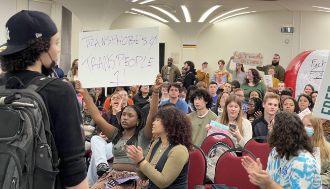 Students gather to protest anti-trans speaker Ian Haworth in the University of Albany's Campus Center; one holds a sign reading "transphobes, 0, trans people, 1."