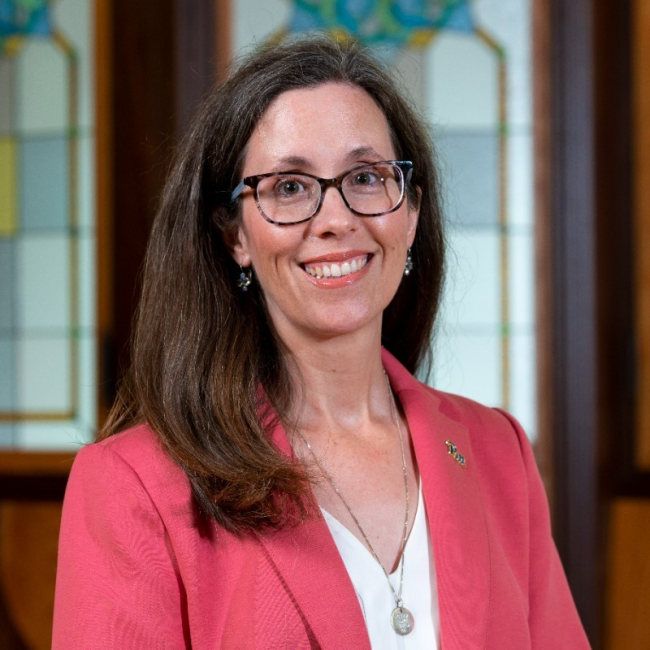 April Belback, a woman with long dark hair who is wearing glasses