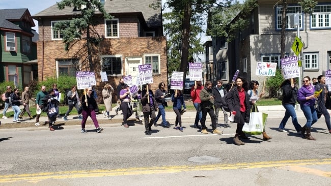 Demonstrators supporting the University of Michigan graduate student workers' strike cross a street, holding signs.