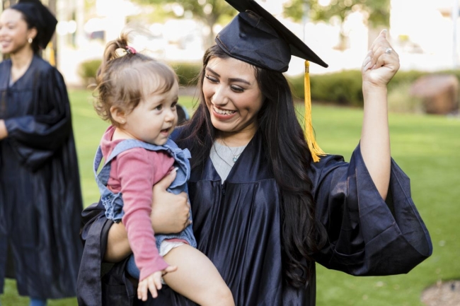 Student parent holding child at college graduation ceremony.