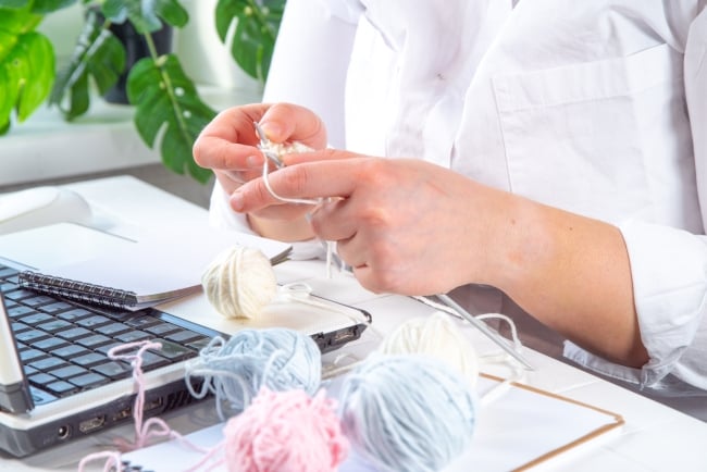 hands knitting over a computer with a ball of yarn to one side