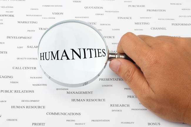 hand holding magnifying glass over the word humanities, which is surrounded by many other words like human resources, management and so forth
