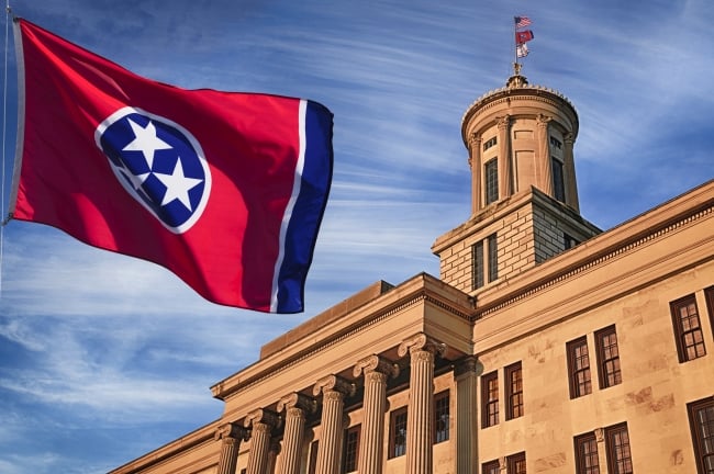 The red and blue Tennessee state flag flies in front of the state capitol building.
