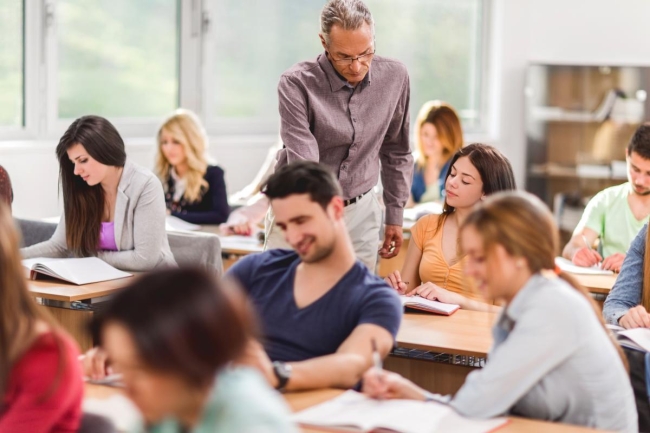 A professor points to a student's textbook while other students around them read.