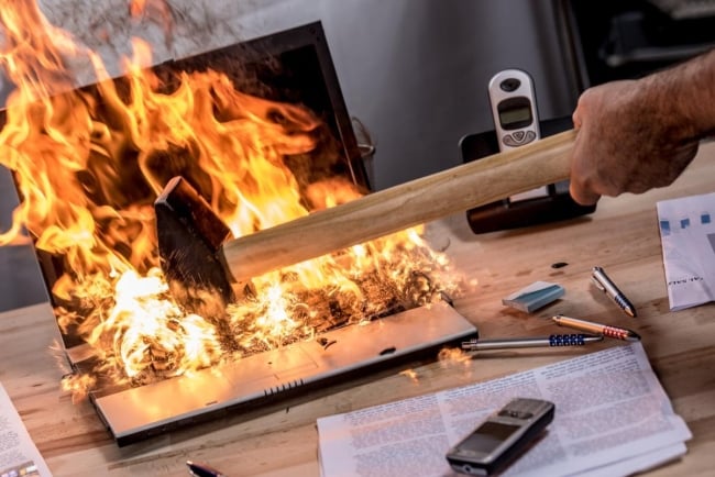 Photo of a hammer blow destroying a flaming laptop computer