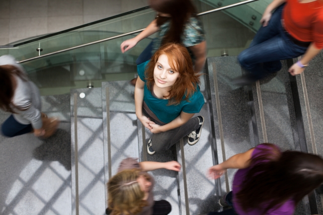A student looks up as she walks on a busy staircase on a campus.