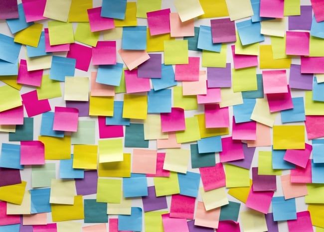 A white wall is covered in blank blue, purple, yellow, orange and green sticky notes.