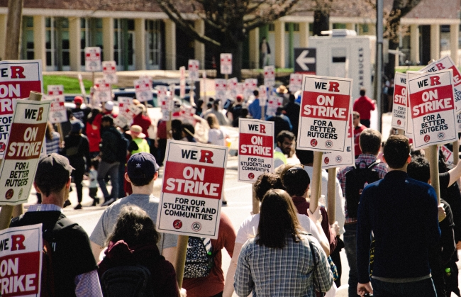 Striking Rutgers union members hold red and white signs