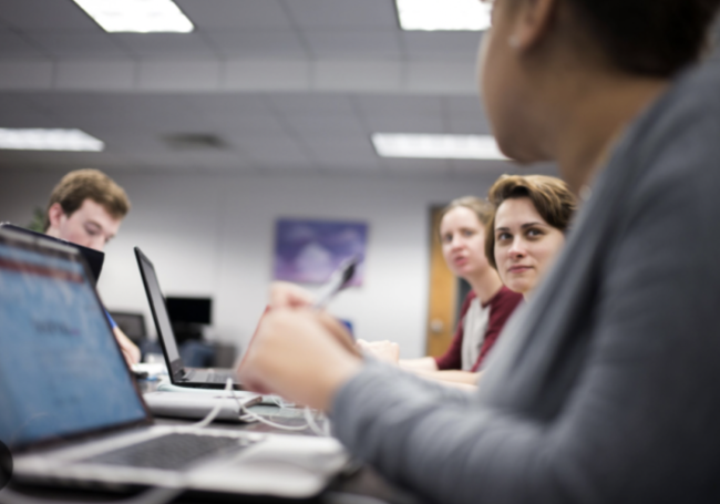 Several Tallahassee Community College students sit at a long table with laptops.