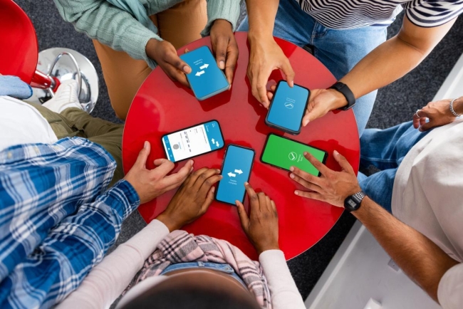 Overhead shot of students sitting around a round table with their smartphones out.