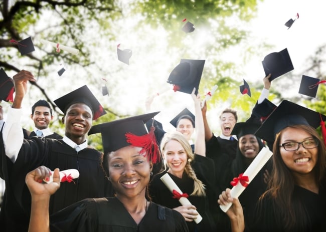 A group of about eight happy graduates, wearing caps and gowns and clutching diplomas while grinning at the camera.