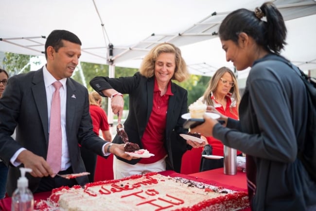 Two college administrators slice a cake that says "Welcome to IU" and hand pieces of cake to students.