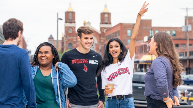 Students in Duquesne University T-shirts stand in a group on campus. 
