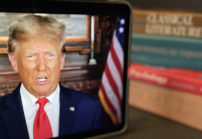 A video of Donald Trump plays on an iPad with college textbooks in the background
