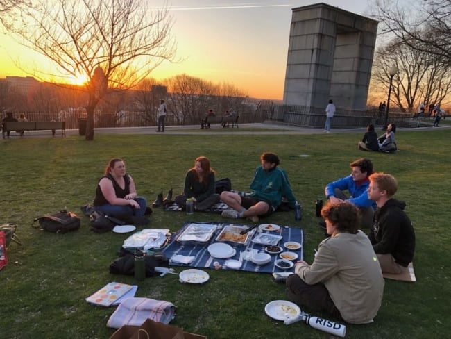 Jewish students at Brown University share a meal in a park as the sun sets.