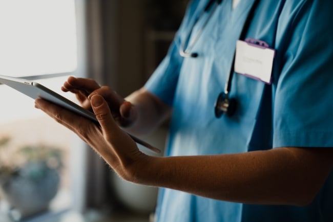 Close-up of female medical professional in scrubs with digital tablet, typing and completing checklist. 