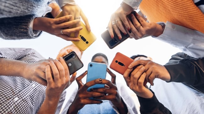 Students are gathered in a circle, all using their cellphones and looking down at the devices.