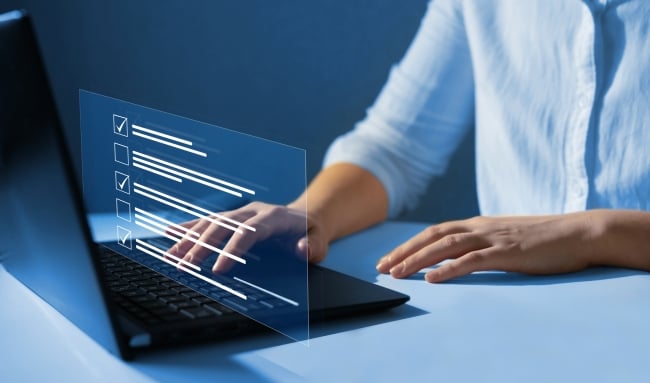 Cropped concept photo of hands on a laptop, filling out some kind of questionnaire. Color scheme is blue.