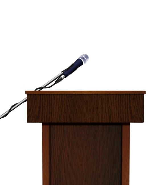 A wooden speaker podium and microphone, against a white background, with no speaker behind it. 