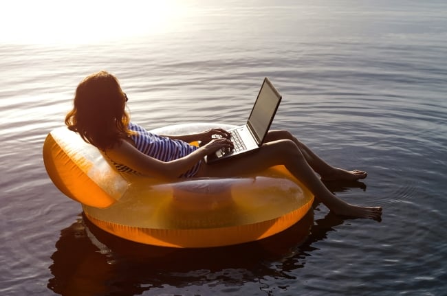 A woman on a flotation device in a body of water working on her laptop.