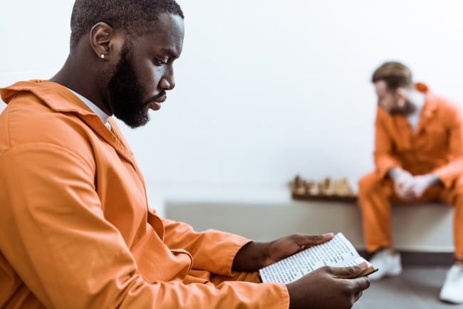 African American man wearing an orange jumpsuit reads a book.