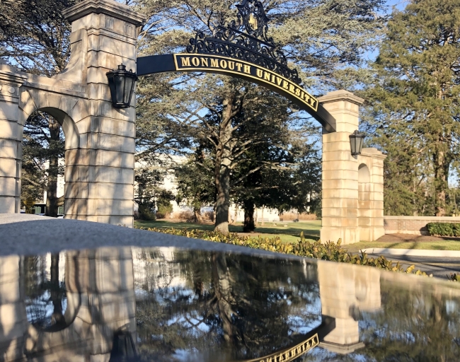 An arching sign reads "Monmouth University" and is reflected in water in the foreground