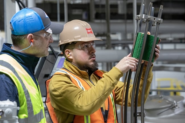 A UW Milwaukee student intern wearing a hard hat and hold equipment during an internship at a drink company