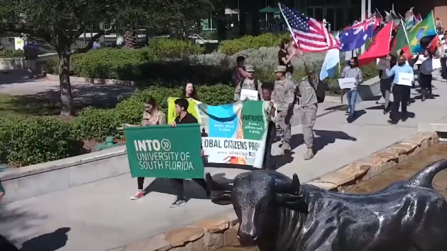 People marching with banners and flags in front of a statue of a bull