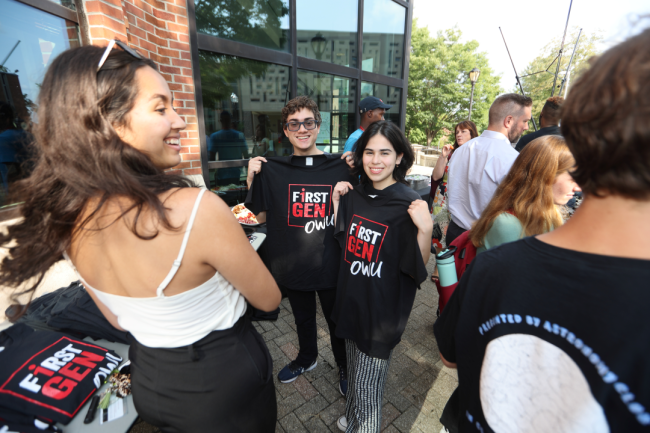 Ohio Wesleyan students smile holding black shirts that say "first-gen OWU"