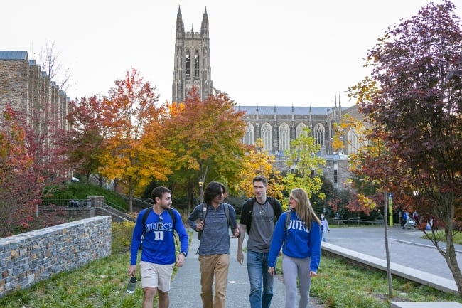 Four Duke students walk down campus in front of the chapel tower.