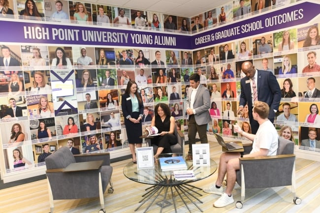 Several people stand around the career center at High Point University, which is adorned with photos of alumni.