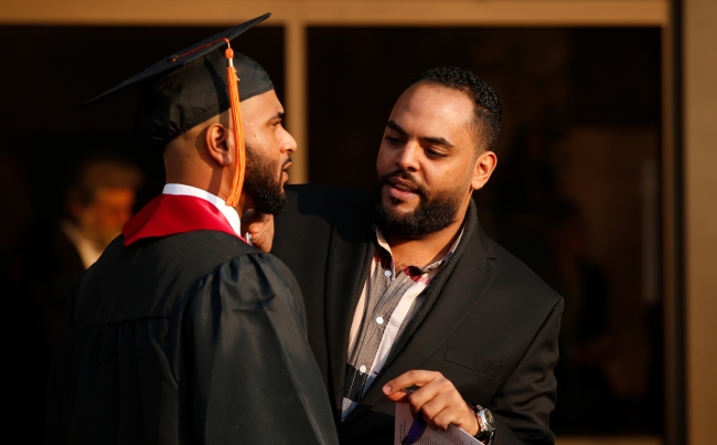 A Black CSU staff member helps a Black student with his graduation regalia