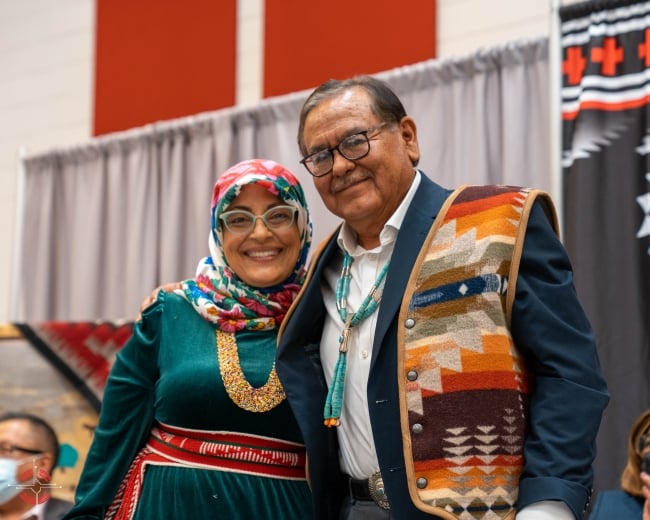 Navajo Technical University president Elmer Guy and Wafa Hozien, university academic administrator, stand together smiling at a campus event celebrating the new Ph.D. program. Both are wearing colorful Native prints. 