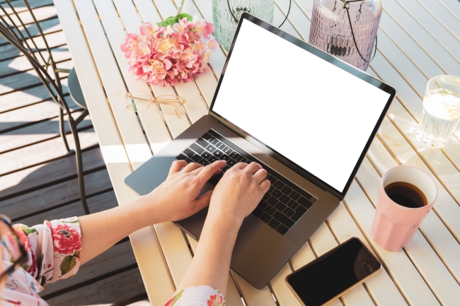 hands of woman writing at a computer on outside table in the summer