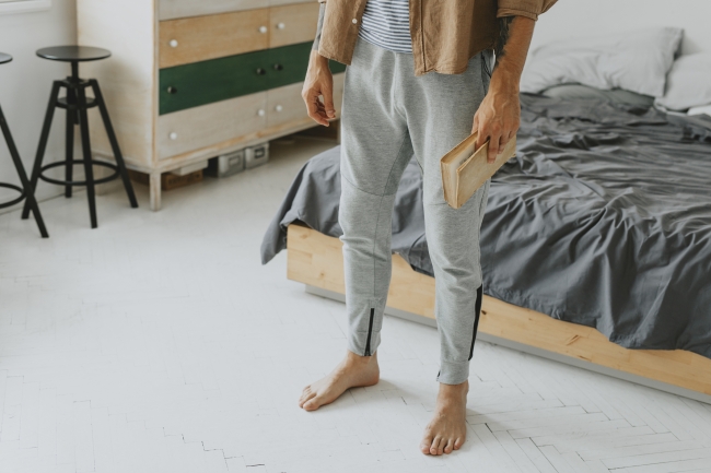 Student in bedroom with messy bed holding a book and wearing sweatpants