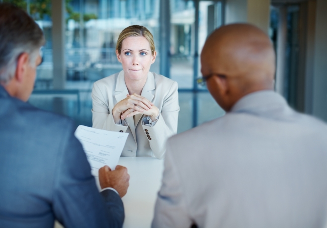 Anxious woman looks at two men interviewers with their backs to the viewer