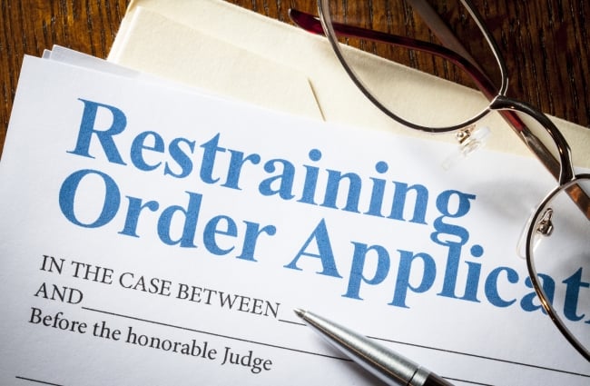 An application for a restraining order, with a pen and a pair of glasses resting on top.