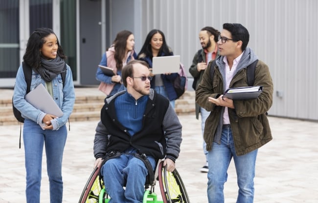 Students carrying books chat on a college campus.