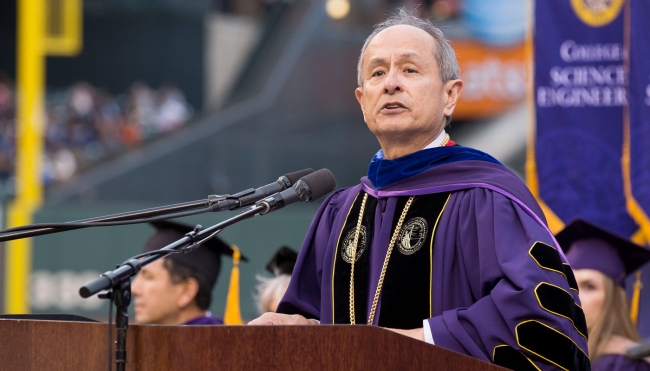 A photo of Les Wong, wearing purple academic regalia, speaking at a college event