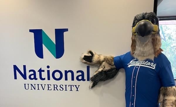 A person wearing a falcon mascot costume poses next to a sign reading "National University."