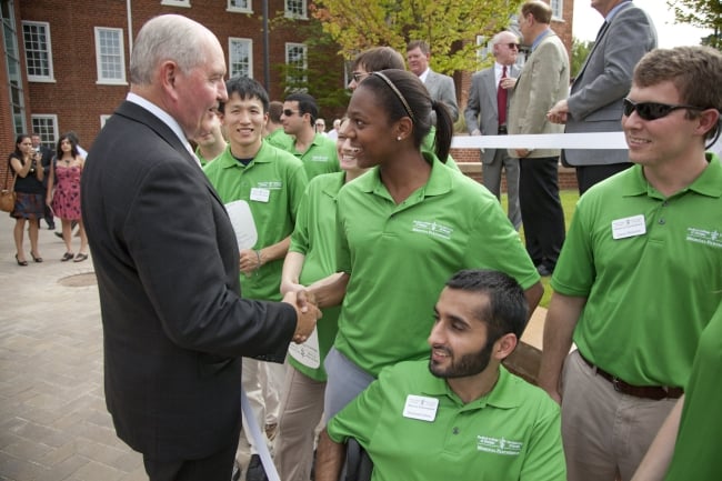 Sonny Perdue, chancellor of the University System of Georgia, shakes hands with a young student in a green T-shirt..