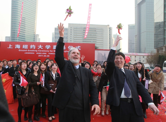 Two men in suits toss garlands behind them to a crowd.
